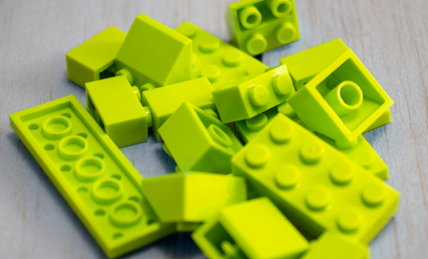 Ein Haufen leuchtend gelbgrüner Plastikbausteine, die an Kreativwerkstätten wie Fortbildung KOMMA Bordesholm erinnern, liegt auf einer hellen Holzfläche verstreut.